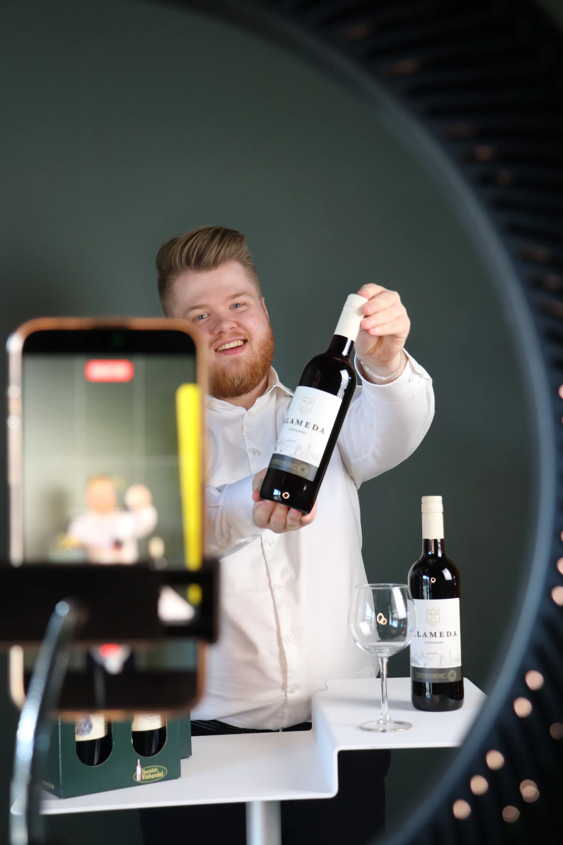 Vinhandler holder live show med ringlys og telefon på stativ