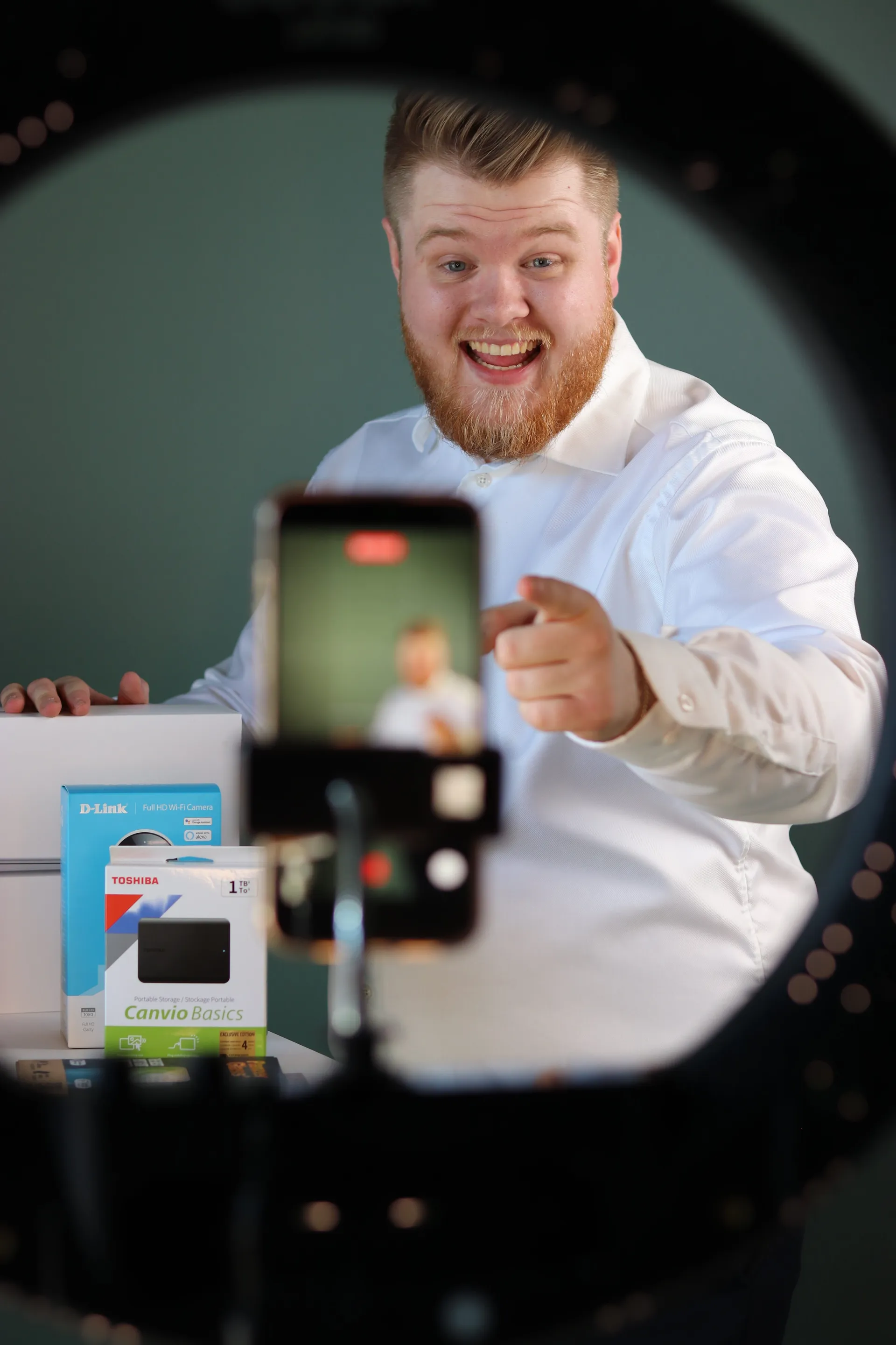 Grinende vært peger på telefonkameraet der filmer live med produkter på bordet