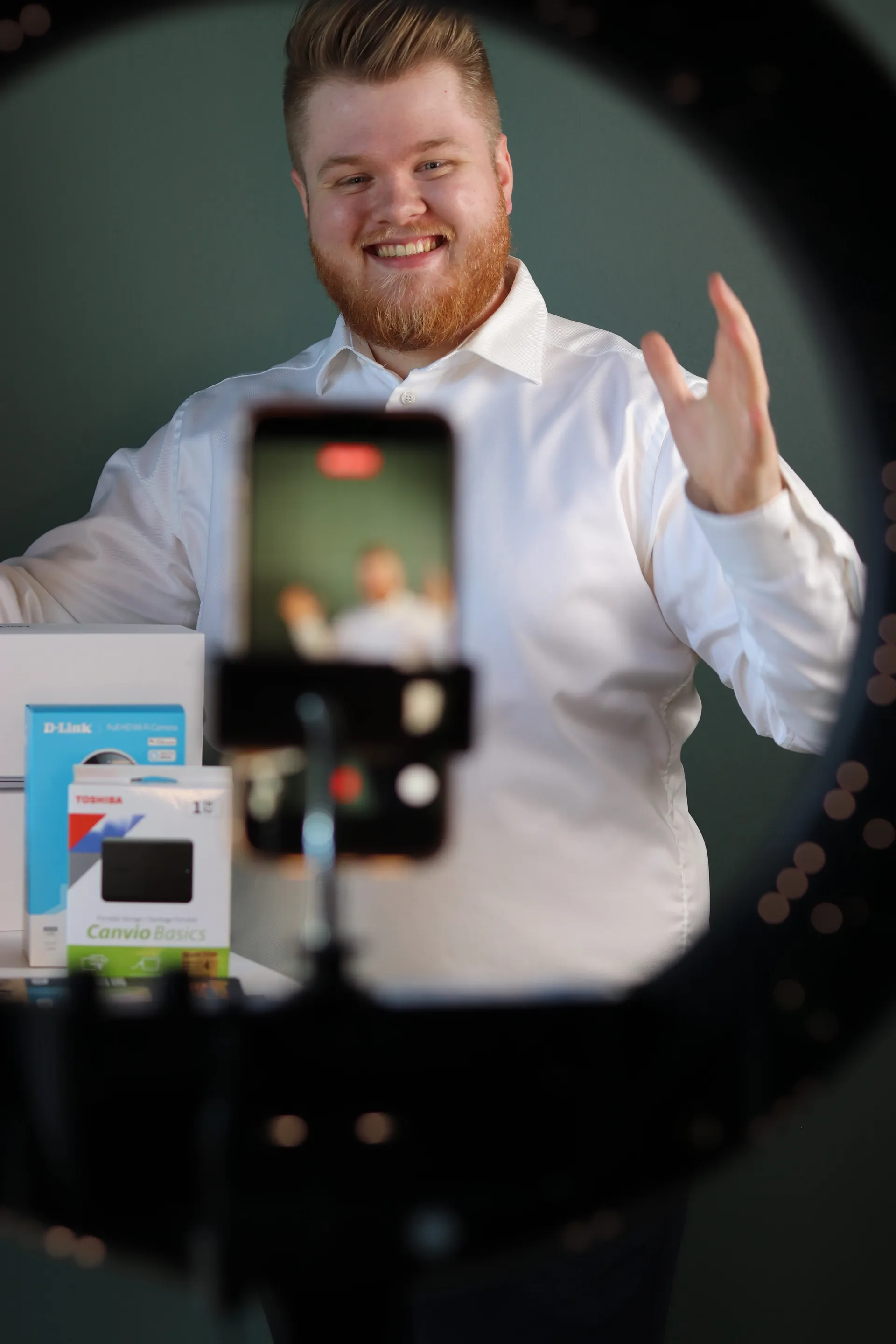 Vært vinker til telefonkameraet under et live show med elektronik på bordet