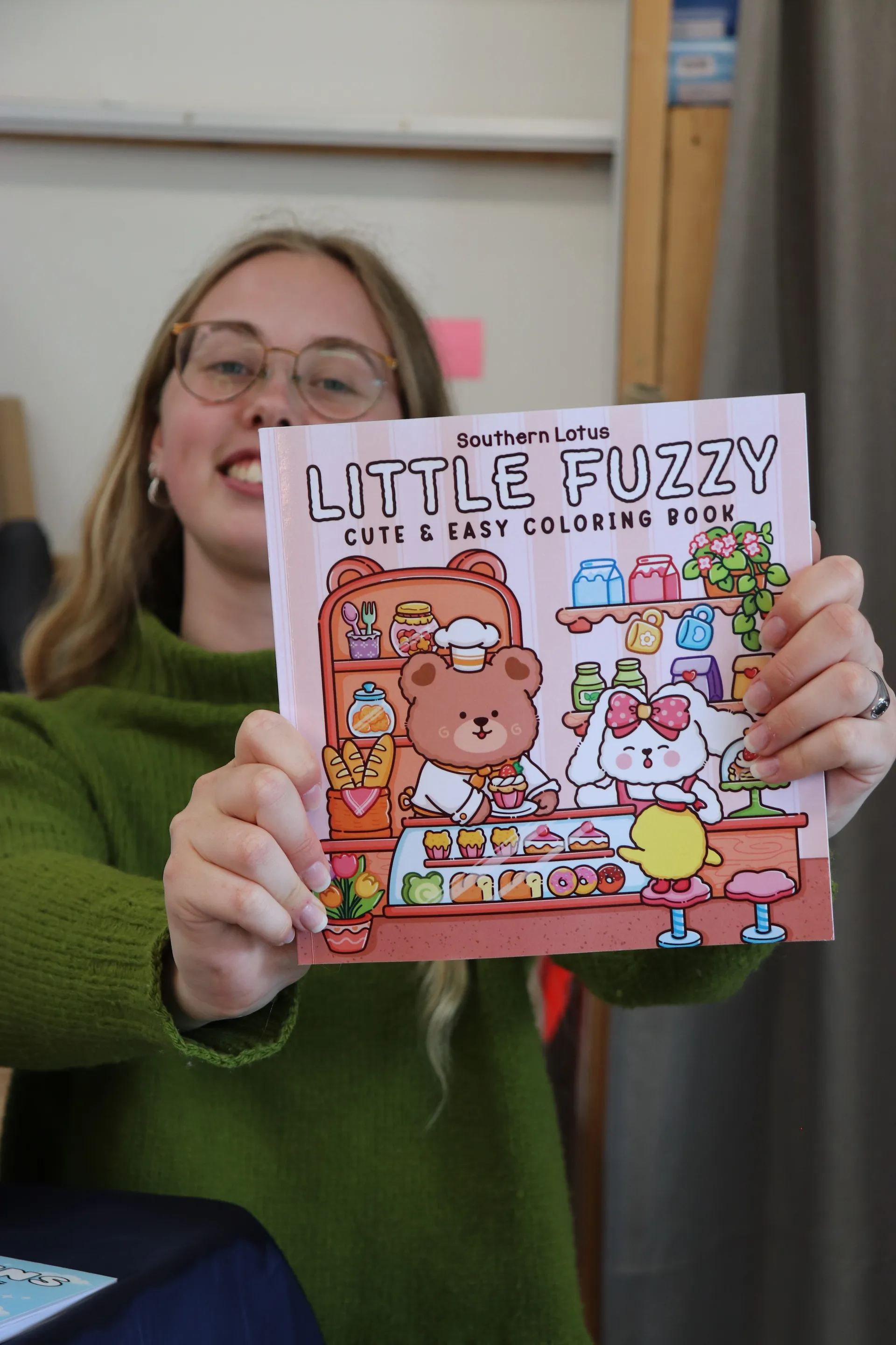 Smilende vært holder en Little Fuzzy Southern Lotus malebog op med forsiden mod kameraet