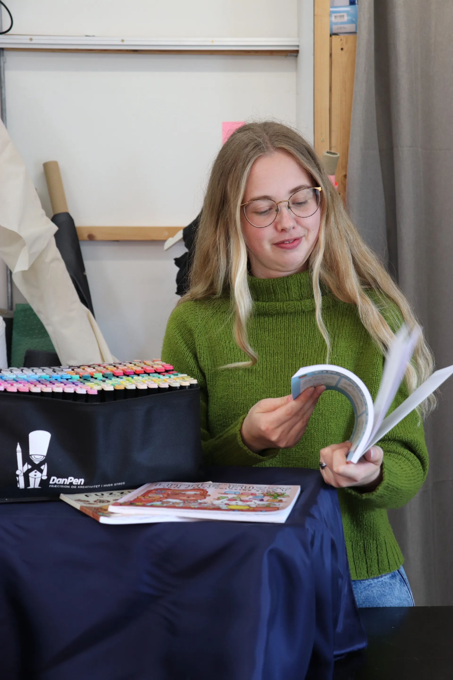 Vært bladrer smilende gennem en malebog med tuscher i baggrunden
