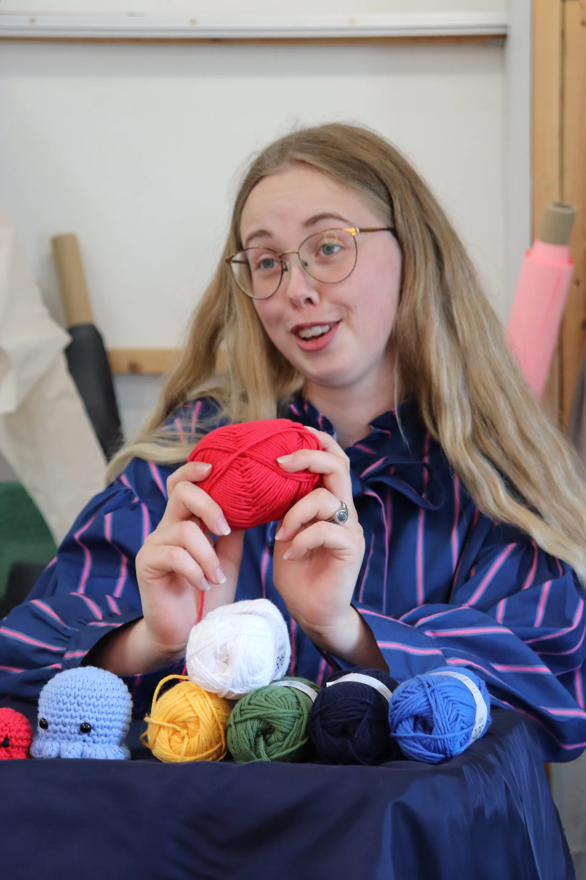 Vært holder et rødt garnnøgle frem med hæklede amigurumi og farverige nøgler på bordet