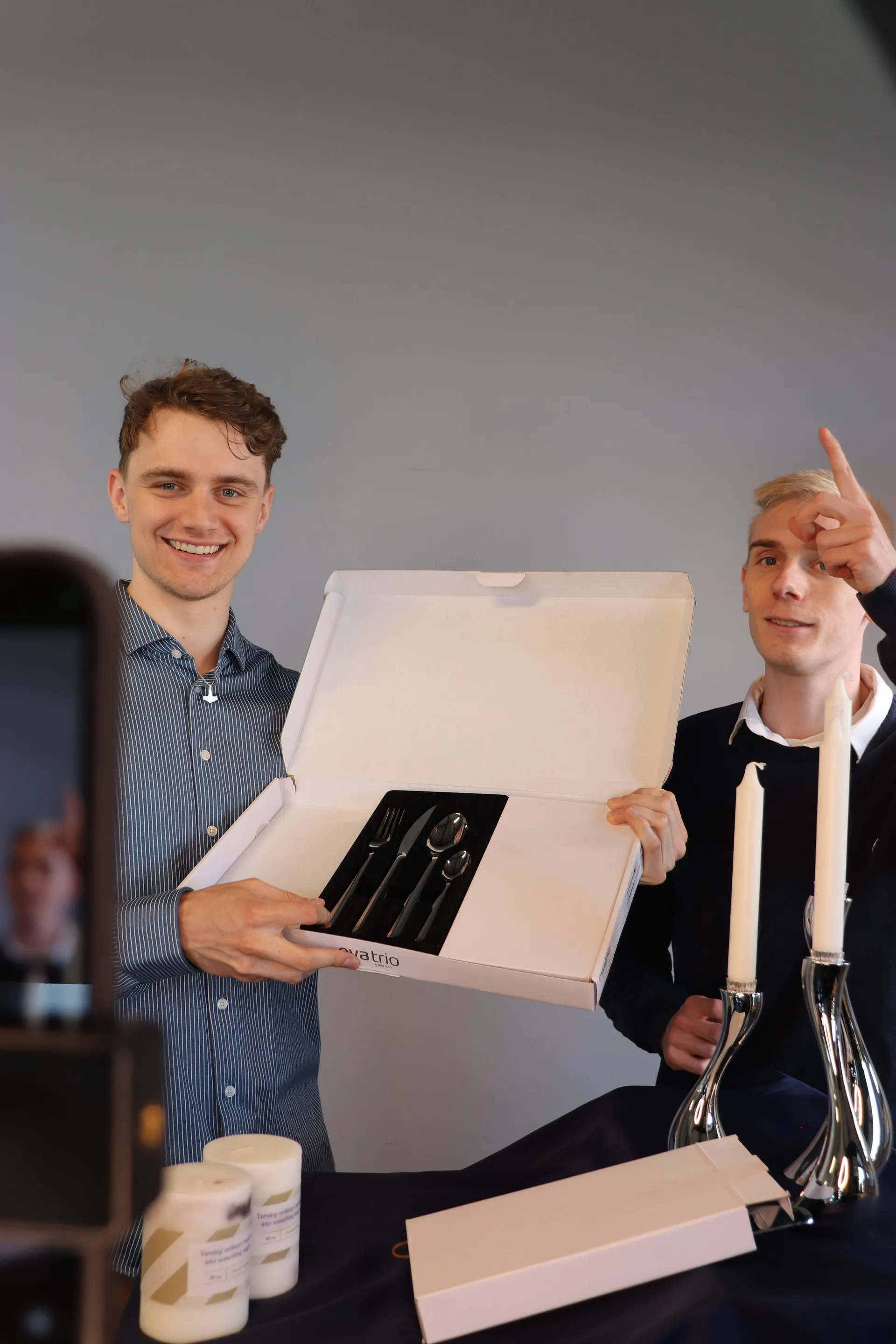 To værter præsenterer en åben æske med bestik under et live show med lysestager på bordet