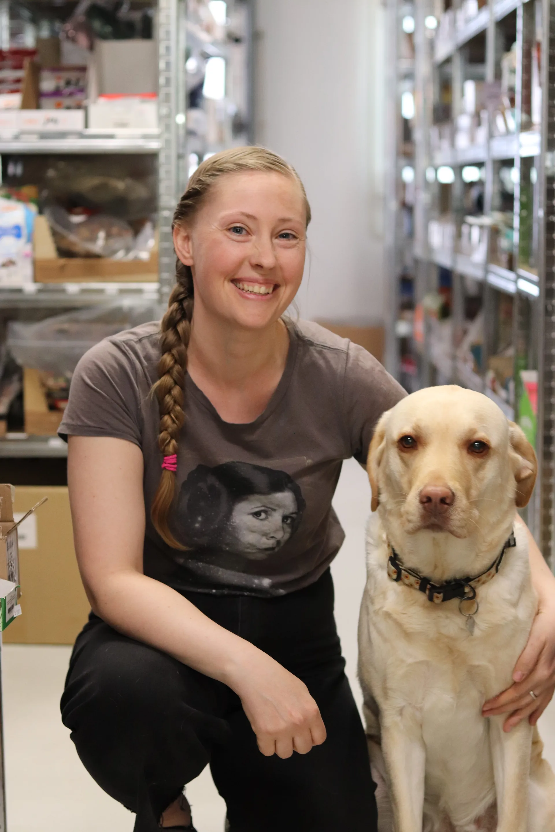 Smilende butiksindehaver sidder på hug ved siden af en gul labrador i butikken